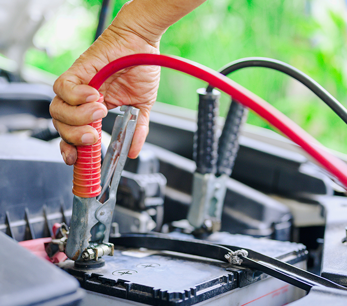a person placing the red jumper cable onto the car battery inside a car 