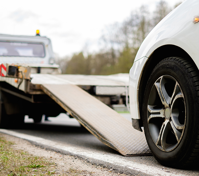 a white car next to a towing truck ready to be loading onto the back of the tow truck