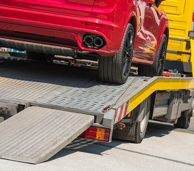 a red car on a yellow towing truck in preparation for transport 