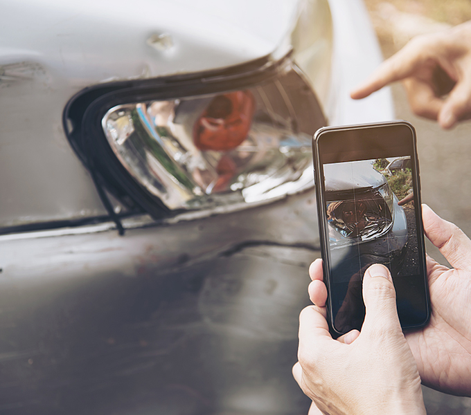 two individuals taking a photo of a damaged car 