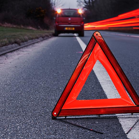 a red car broken down on the side of a road with a triangular breakdown sign behind it